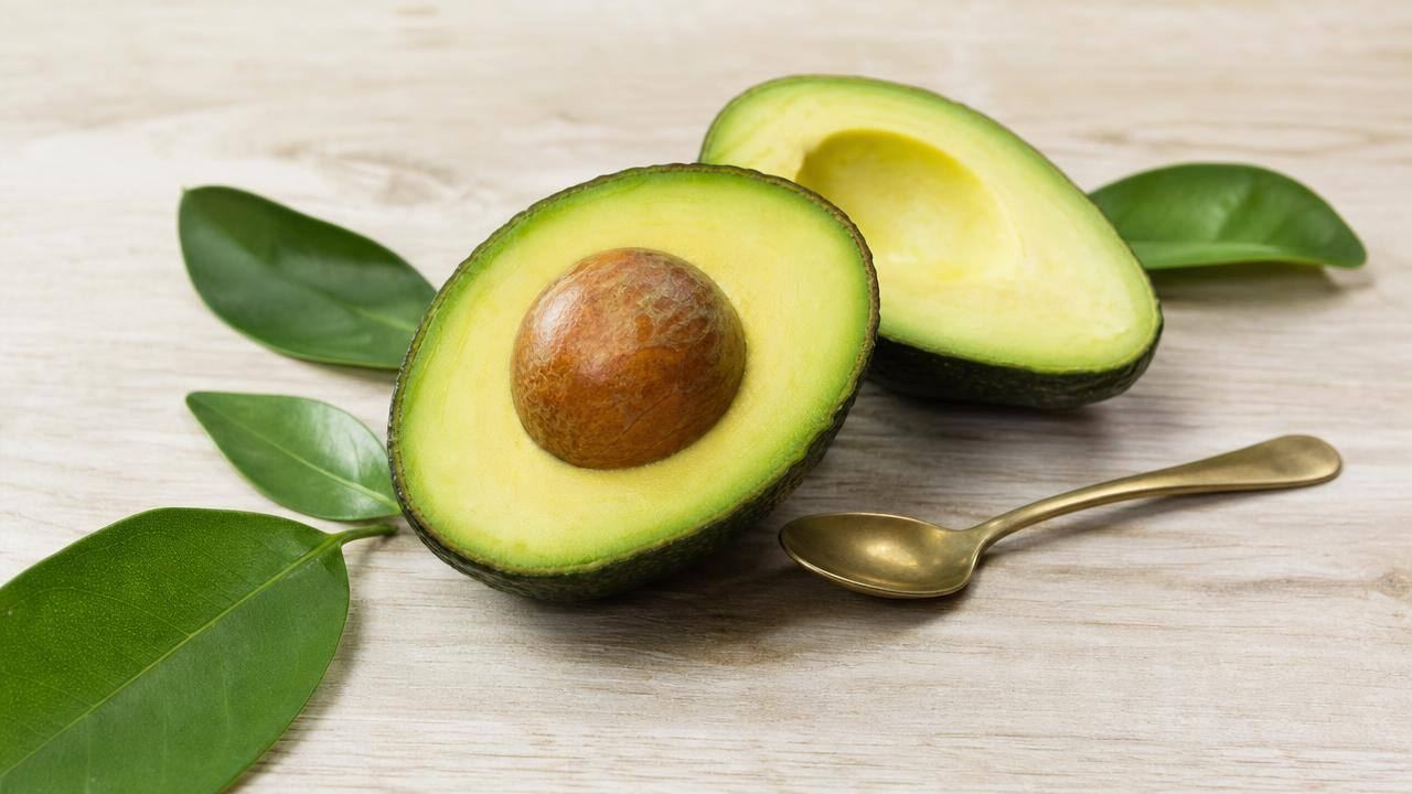 Abacate cortado ao meio com polpa verde sobre uma mesa clara, ao lado de ingredientes naturais