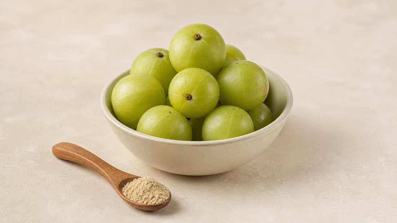 Fruta amalaki verde em uma tigela clara, com pó de amla ao lado, em composição editorial limpa