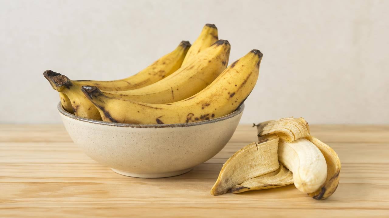 Bananas maduras em uma tigela de cerâmica sobre mesa clara, em composição limpa e editorial