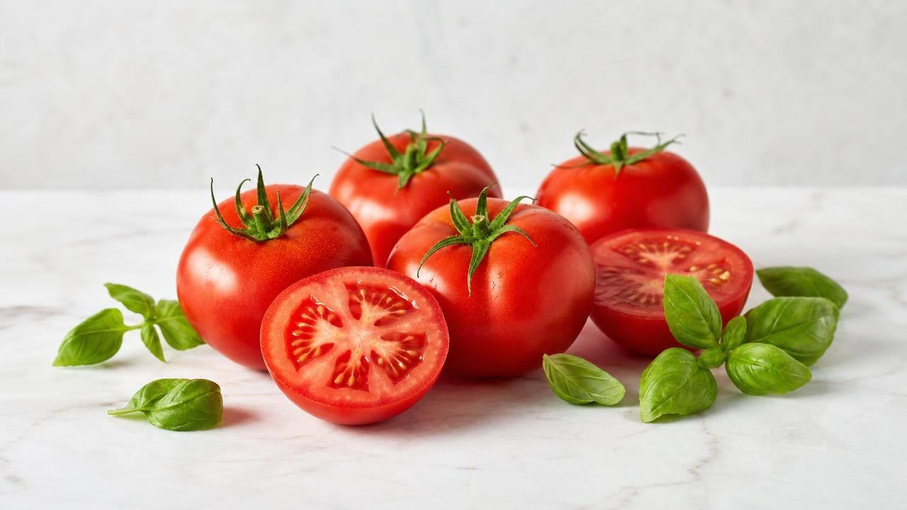 Tomates frescos inteiros e cortados sobre superfície clara, com folhas de manjericão e composição limpa
