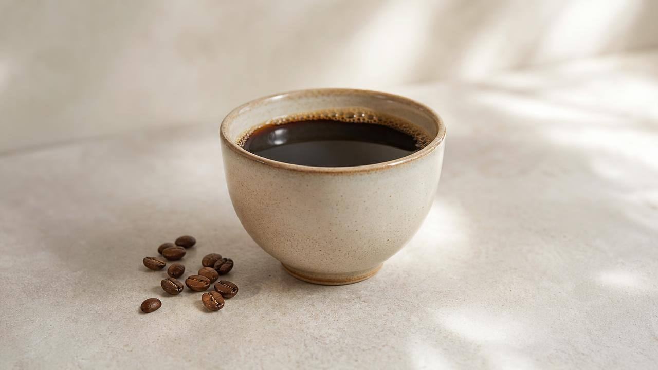 Xícara de café coado preto sobre mesa clara, em composição editorial minimalista