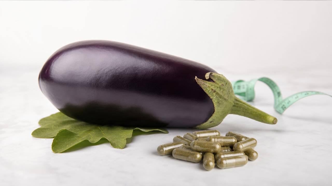 Cápsulas vegetais ao lado de uma berinjela fresca e fita métrica em fundo claro