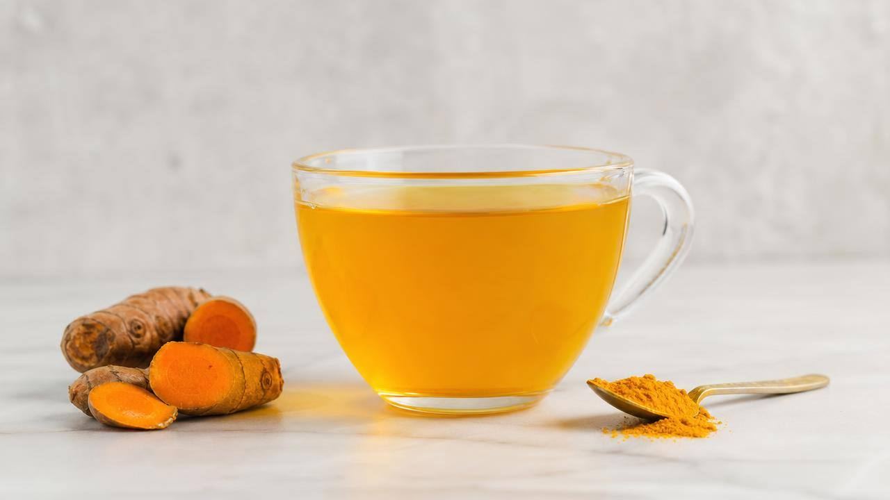 Xícara de chá de cúrcuma com raiz de açafrão-da-terra e pó amarelo sobre mesa clara