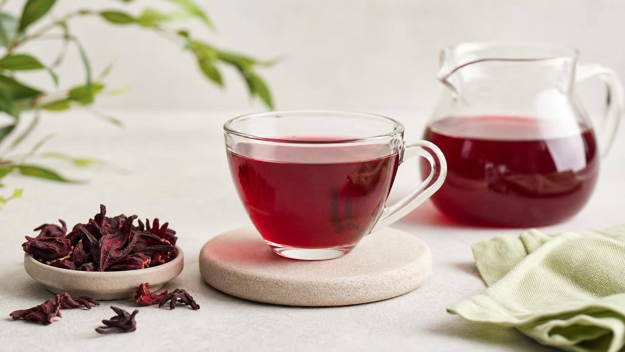 Xícara de chá de hibisco vermelho ao lado de cálices secos de hibisco, em fundo claro e minimalista