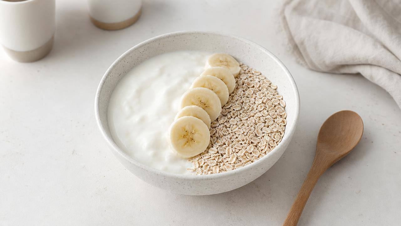 Tigela de iogurte natural com farelo de aveia, banana fatiada e colher de madeira