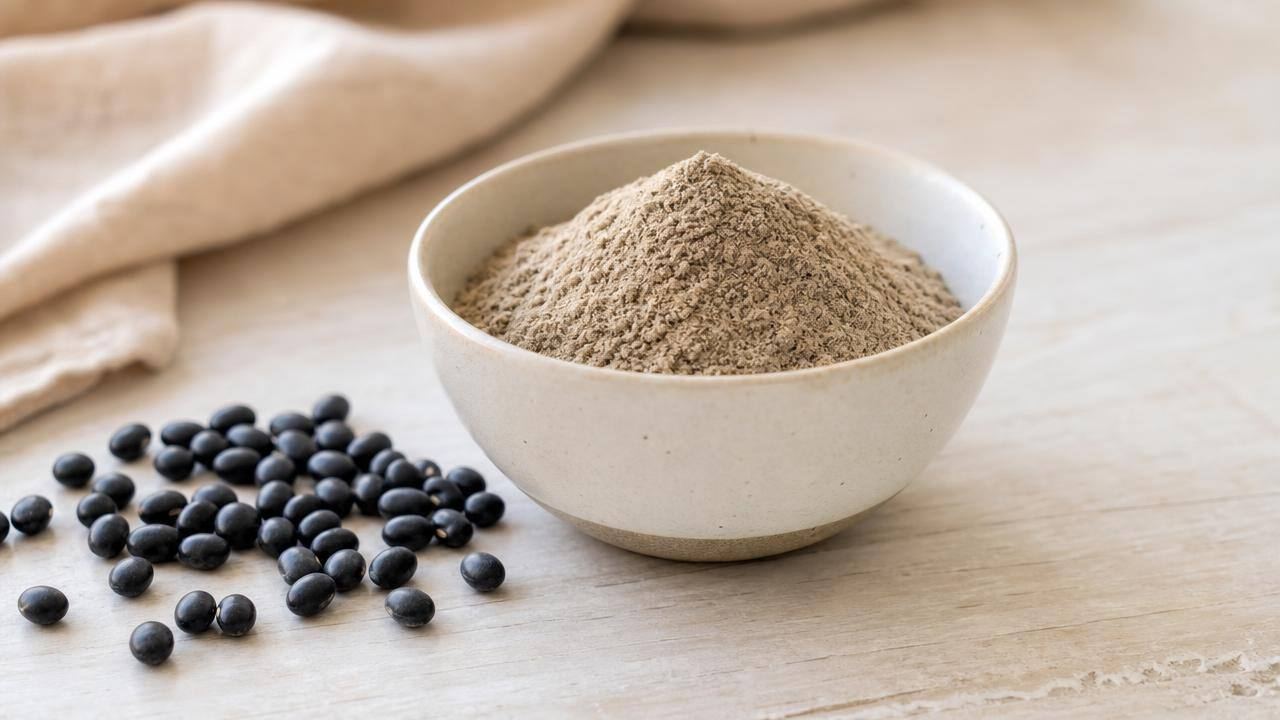 Tigela com farinha de soja preta e grãos de soja preta sobre mesa clara, em composição editorial limpa