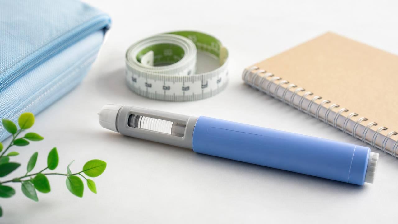 Caneta aplicadora de medicamento injetável ao lado de itens de acompanhamento de saúde, em composição limpa e profissional