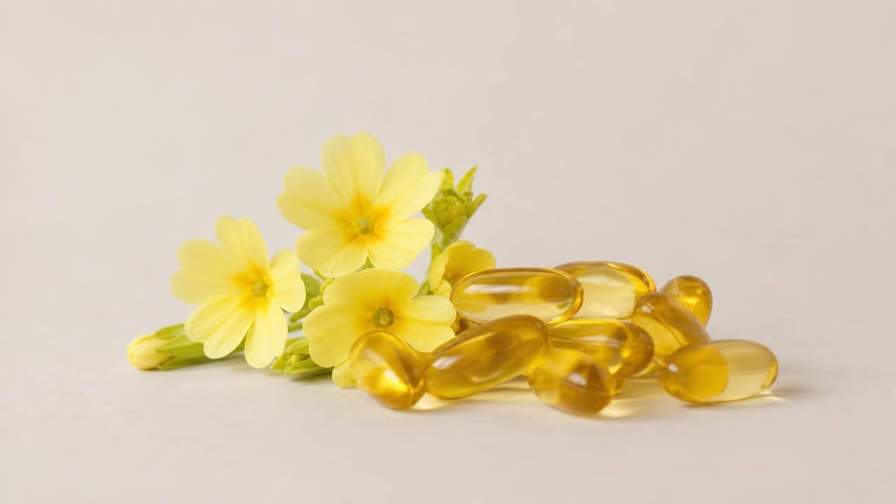 Cápsulas de óleo de prímula ao lado de flores amarelas de prímula em composição limpa