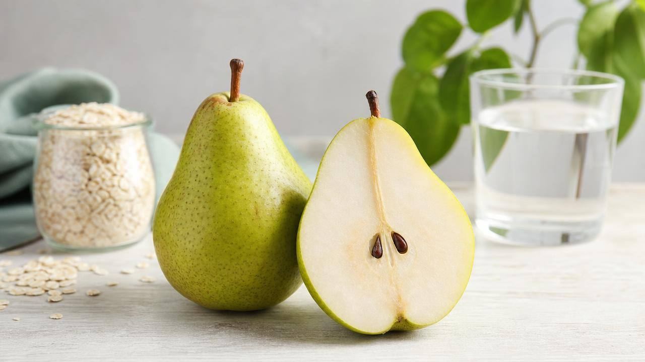 Pera fresca cortada ao meio sobre uma mesa clara, acompanhada de aveia e um copo de água
