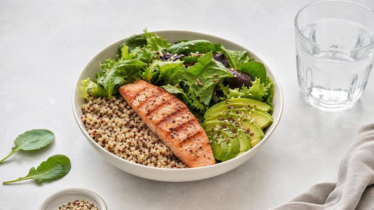 Prato equilibrado com quinoa, salmão, folhas verdes, abacate e sementes em uma mesa clara