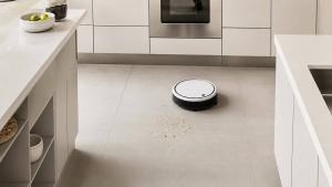 Aspirador robô próximo a pequenas migalhas secas no piso de uma cozinha limpa e moderna