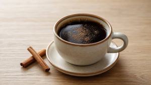 Ilustração de Xícara de café preto com canela em pó e paus de canela sobre uma mesa clara