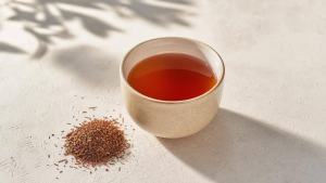 Ilustração de Xícara de chá de rooibos em mesa clara, com folhas secas ao lado