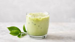 Copo de chá verde gelado batido com iogurte natural, servido ao lado de folhas de chá em uma mesa clara