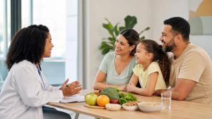 Profissional de saúde conversando com uma família sobre alimentação equilibrada em ambiente clínico claro e acolhedor