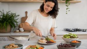 Pessoa montando um prato equilibrado com legumes, arroz, feijão e proteína em uma cozinha clara