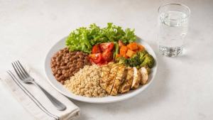 Ilustração de Prato equilibrado com arroz integral, feijão, frango grelhado, salada e água, representando uma alimentação para desinchar com equilíbrio