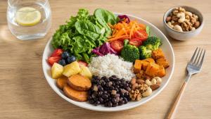 Ilustração de Prato equilibrado com folhas verdes, legumes, arroz, feijão, frutas e castanhas sobre mesa clara