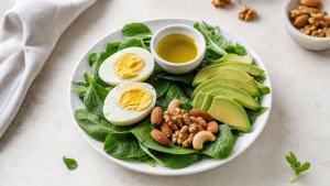 Prato equilibrado com ovos, folhas verdes, abacate, azeite e castanhas em uma mesa clara