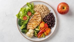 Prato equilibrado com legumes, feijão, arroz integral, peixe e frutas, representando uma dieta para colesterol alto