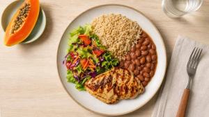 Prato equilibrado com arroz, feijão, frango grelhado, salada e frutas em uma mesa clara