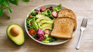 Ilustração de Abacate cortado ao lado de uma salada colorida e uma torrada integral em mesa clara