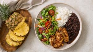 Abacaxi fresco cortado ao lado de prato equilibrado com salada, arroz, feijão e proteína