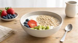 Tigela de iogurte natural morno com aveia e frutas frescas em mesa clara