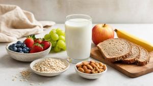 Copo de leite, frutas, aveia e outros alimentos naturais dispostos em mesa clara, representando uma alimentação equilibrada