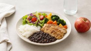 Refeição fitness equilibrada com arroz, feijão, frango, legumes e frutas em uma mesa clara