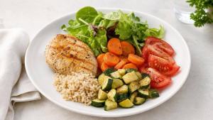 Prato equilibrado com frango grelhado, legumes coloridos e salada em mesa clara