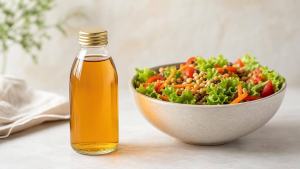 Frasco de vinagre de maçã ao lado de salada colorida com folhas, tomate e grãos em mesa clara