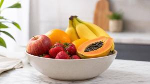 Bowl centralizado com maçã, banana, mamão, morangos e laranja frescos sobre mesa clara