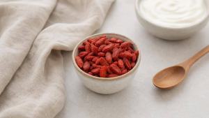 Tigela com goji berry desidratada sobre mesa clara, acompanhada de iogurte natural e colher