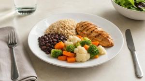 Ilustração de Prato de jantar equilibrado com legumes, arroz integral, feijão e frango grelhado em mesa clara
