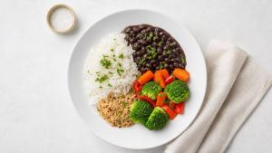 Prato caseiro com legumes, arroz, feijão, ervas frescas e pequeno recipiente de sal, representando o uso moderado de sal na dieta