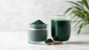 Pote de spirulina em pó ao lado de colher medidora e copo com bebida verde, em composição limpa e editorial