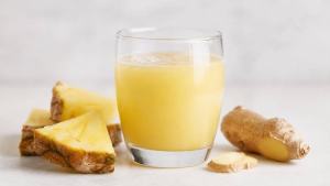 Copo de suco de abacaxi com gengibre ao lado de fatias de abacaxi e gengibre fresco