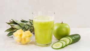 Ilustração de Copo de suco verde-claro de abacaxi, pepino e maçã com ingredientes frescos ao lado em fundo claro