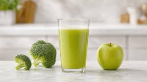 Copo de suco verde de brócolis com maçã ao lado de floretes de brócolis e uma maçã fresca