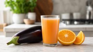 Copo de suco de berinjela com laranja ao lado de berinjela fresca e laranjas cortadas