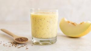Copo de suco de melão com linhaça moída, sementes de linhaça e fatias de melão sobre mesa clara