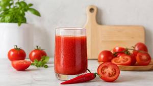 Copo de suco de tomate caseiro com pimenta ao lado de tomates frescos e uma pimenta vermelha