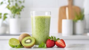 Copo de suco verde com frutas frescas, kiwi, morangos e folhas de hortelã sobre bancada clara